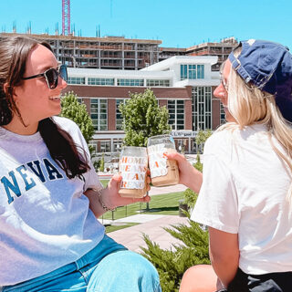 Two young women sitting on the sidewalk in front of a blue wall with 'BATTLE BORN' painted in white
